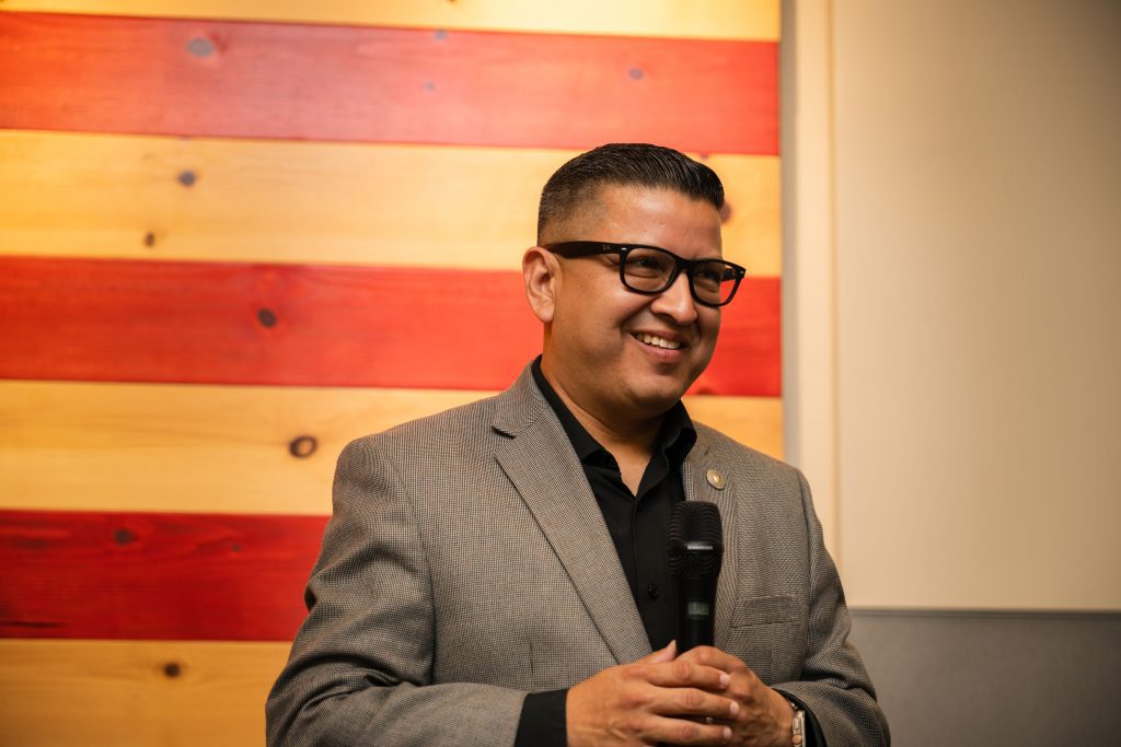 Jesse Armendarez in front of wooden art work holding a microphone and smiling