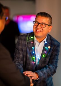 Jesse Armendarez shaking someone's had with a necklace with lit Christmas lights on.