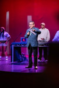 Jesse Armendarez on stage in a suit holding a folder and a microphone