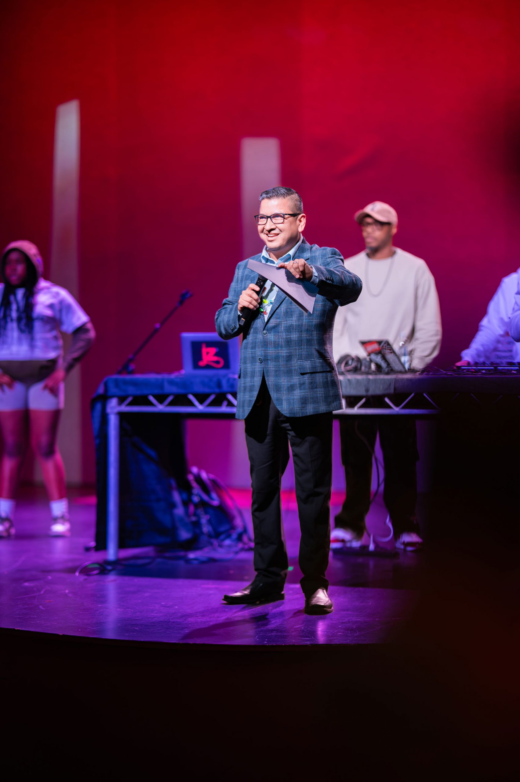 Jesse Armendarez on stage in a suit holding a folder and a microphone