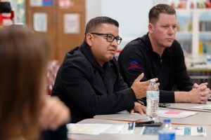 Jesse Armendarez sitting at a table with papers in front of him and a man next to him.