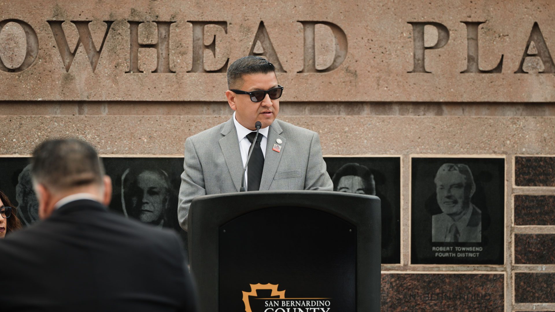 Jesse Armendarez speaking at podium in front of the Arrowhead Plaza.