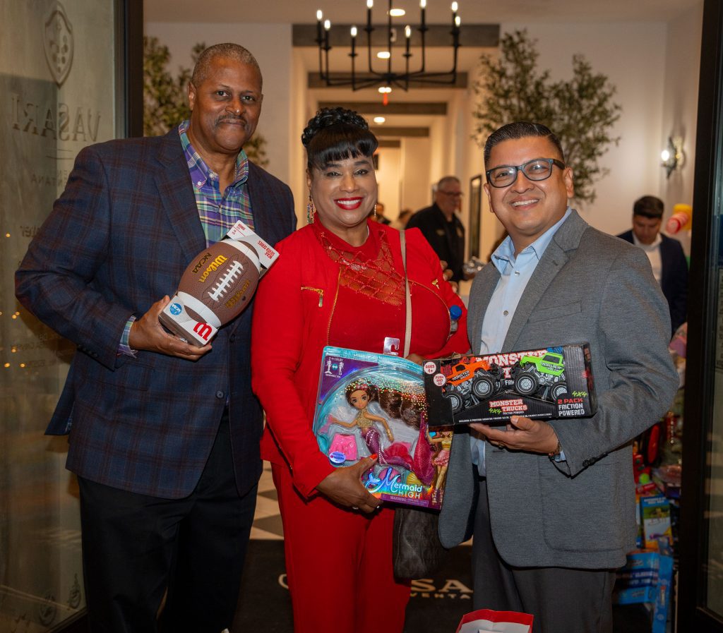 Jesse Armendarez holding a monster truck toy next to a woman and man whom are also holding children's toys and smiling.