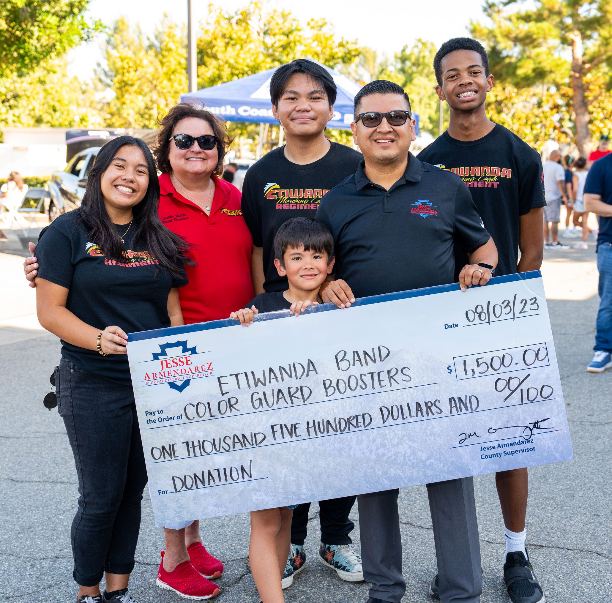 Jesse Armendarez standing with kids and a woman holding a large check of 1,500 dollars for the Etiwanda band color guard boosters.
