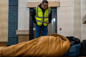 Jesse Armendarez standing in a high visibility vest looking at a person in a sleeping bag.
